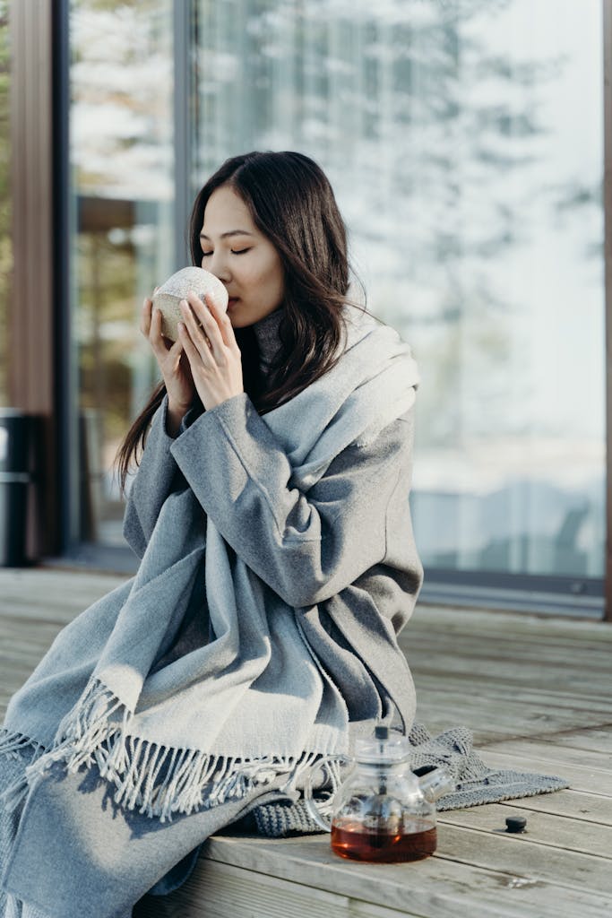 Asian woman wrapped in a scarf sipping a hot beverage outside on a chilly day.
