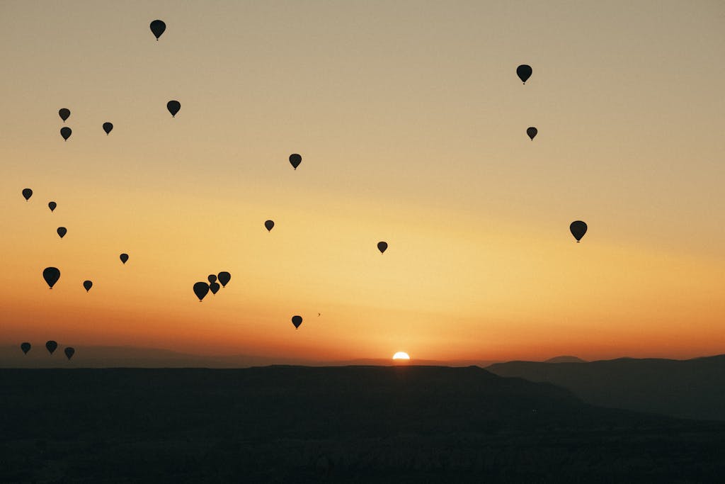 Silhouettes of hot air balloons over Cappadocia at sunrise, offering a serene travel experience.